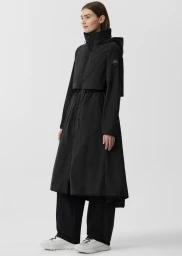 Model Megan Devine wearing a long black Canada Goose parka and white sneakers against a bright studio background.