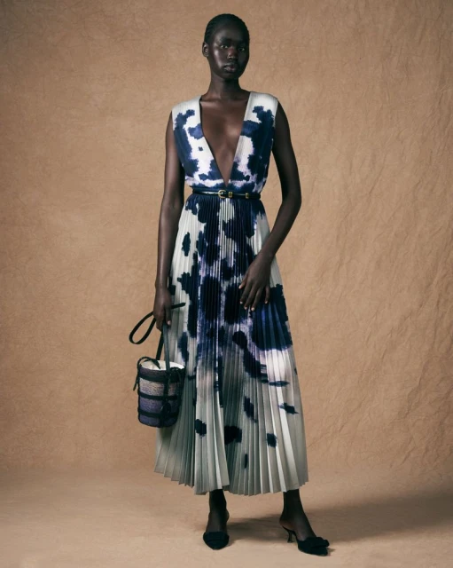 Fashion model poses in full-length shot wearing a sleeveless V-neck dress with black and white tie-dye design, with black heels.
