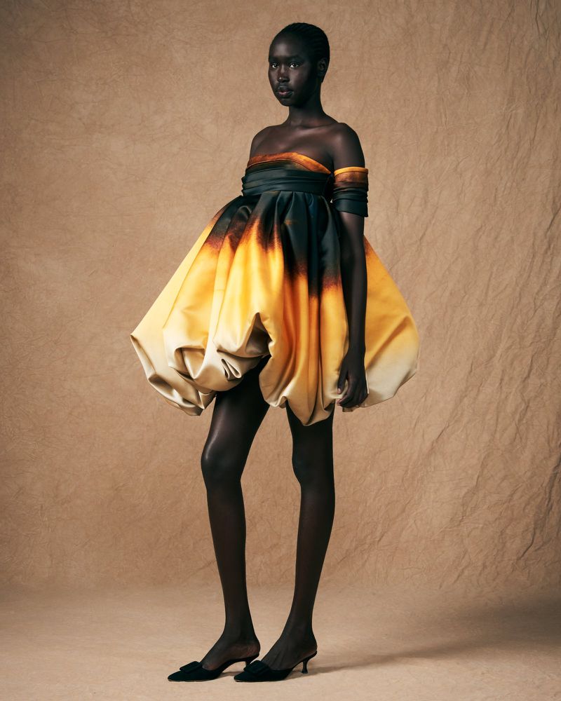 Striking fashion shot of an African woman in a yellow and black couture dress, standing in a studio with a neutral background, showcasing haute couture.