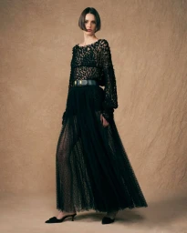 Model wearing a long black textured dress with a belt against a warm brown textured background