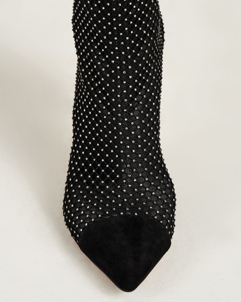 Close-up of a black pointed-toe stiletto bootie featuring a mesh fabric adorned with silver studs on a white background.