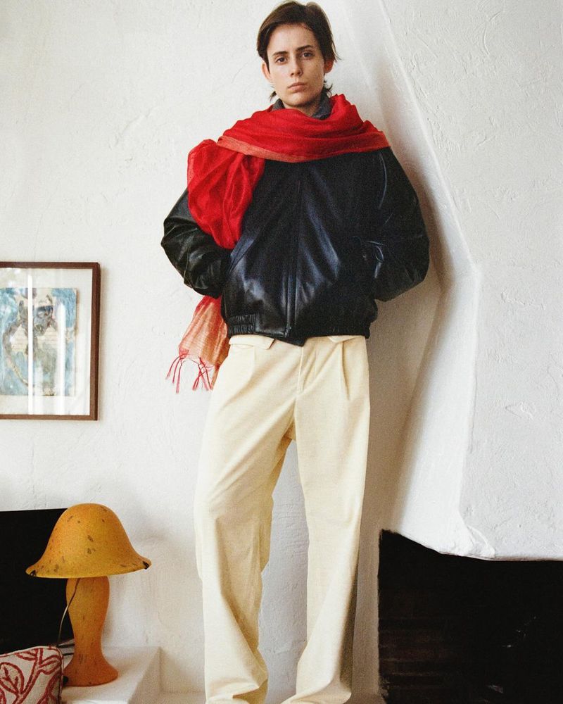 Adult wearing a red scarf and black jacket in an indoor setting with neutral color walls, accented by a lamp and framed art.