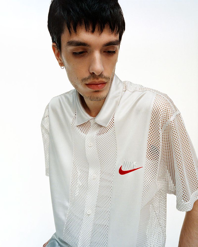 Man in white Nike mesh shirt with red logo against a white background, looking down with a neutral expression.