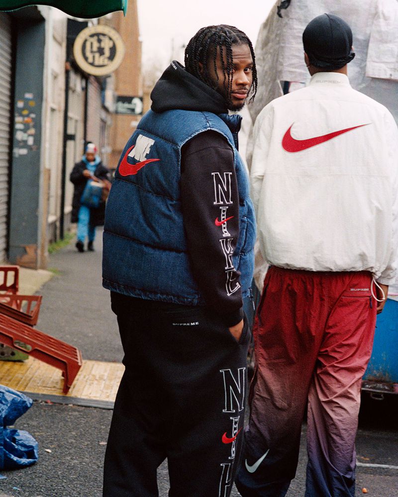 Two people in streetwear style in an urban setting. Person wearing a denim vest and black pants, other person wears a white jacket.