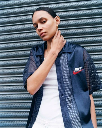 Woman in a navy mesh-paneled Nike top poses against a textured metal wall, showcasing fashion and athletic wear.