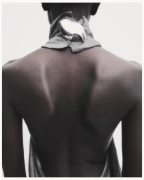 Close-up back view of a model wearing a high-collared grey garment adorned with a large metallic silver brooch