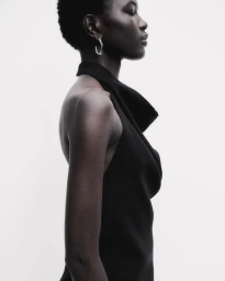 Profile of Nyaduola Gabriel wearing a black cowl-neck sleeveless top and silver hoop earring against a white backdrop.