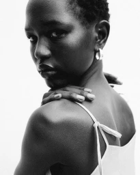 Black-and-white portrait of model Nyaduola Gabriel looking over her shoulder wearing a strap dress and hoop earring
