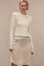 Model Elisa Nijman wearing an off-white long-sleeve top and sheer embellished skirt against a neutral backdrop for H&M.