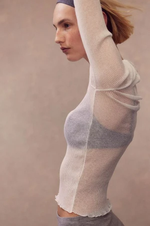 Model Elisa Nijman in side profile wearing a sheer off-white ribbed knit top and grey headband against a neutral studio backdrop.