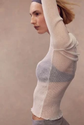Model Elisa Nijman in side profile wearing a sheer off-white ribbed knit top and grey headband against a neutral studio backdrop.