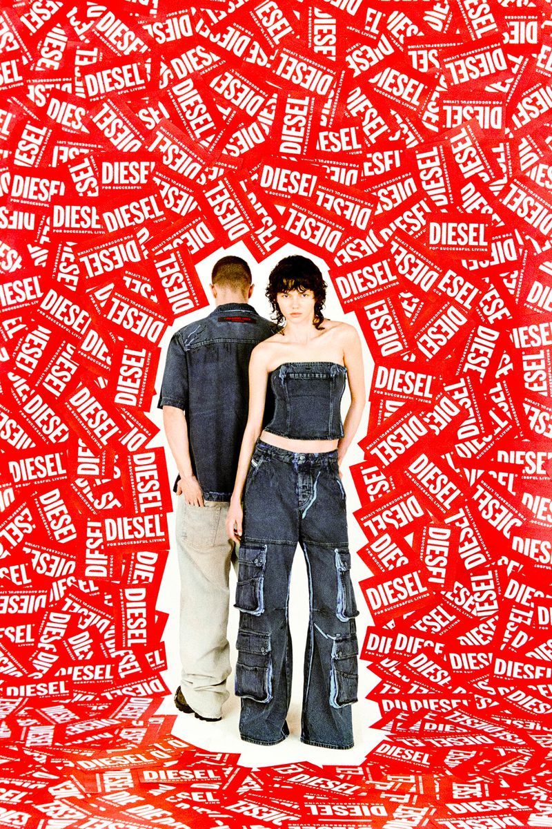 Fashion shot of a couple in denim outfits against a backdrop of red and white Diesel logo tags, showcasing streetwear and brand identity.