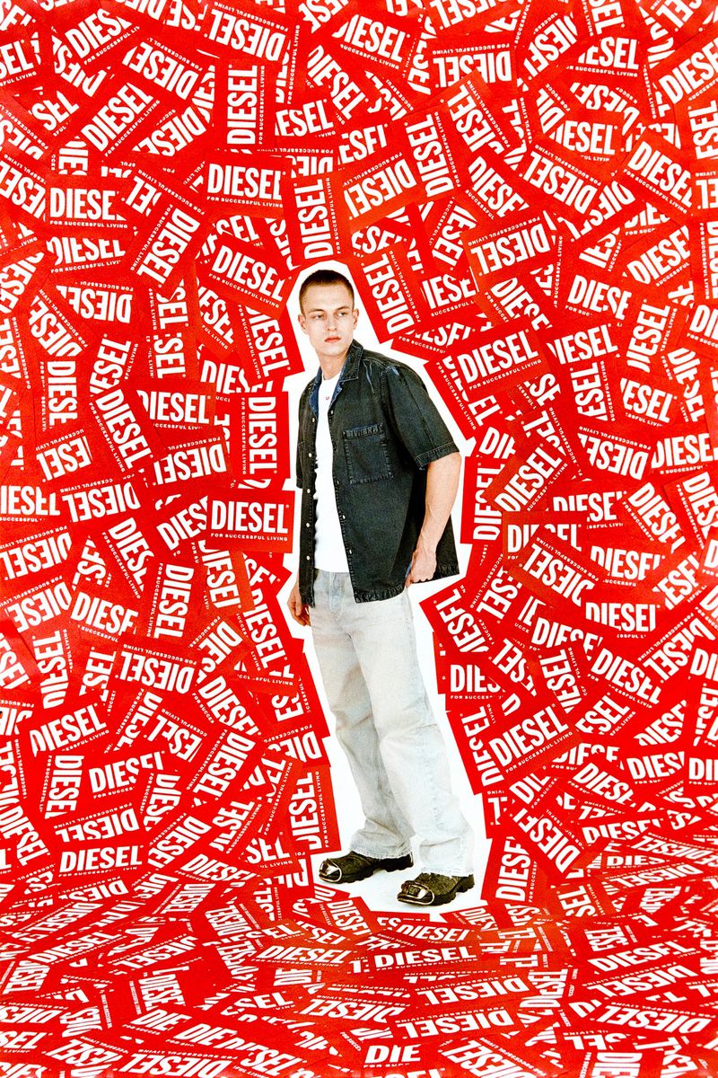 A young adult male stands in an indoor setting, surrounded by scattered Diesel logo cards against a red background, wearing casual clothing.