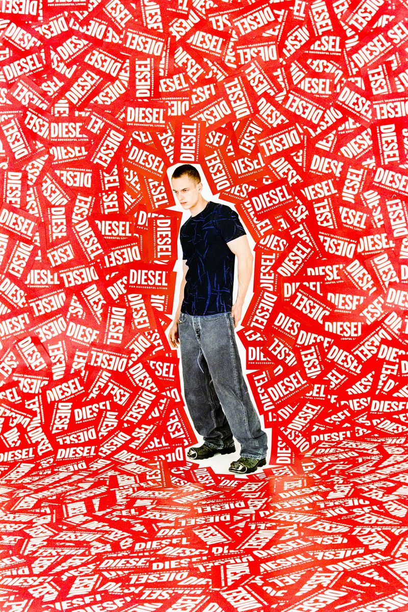 Full-length studio shot of a young adult man in a black shirt and jeans posing against a background covered in red and white Diesel logo stickers.