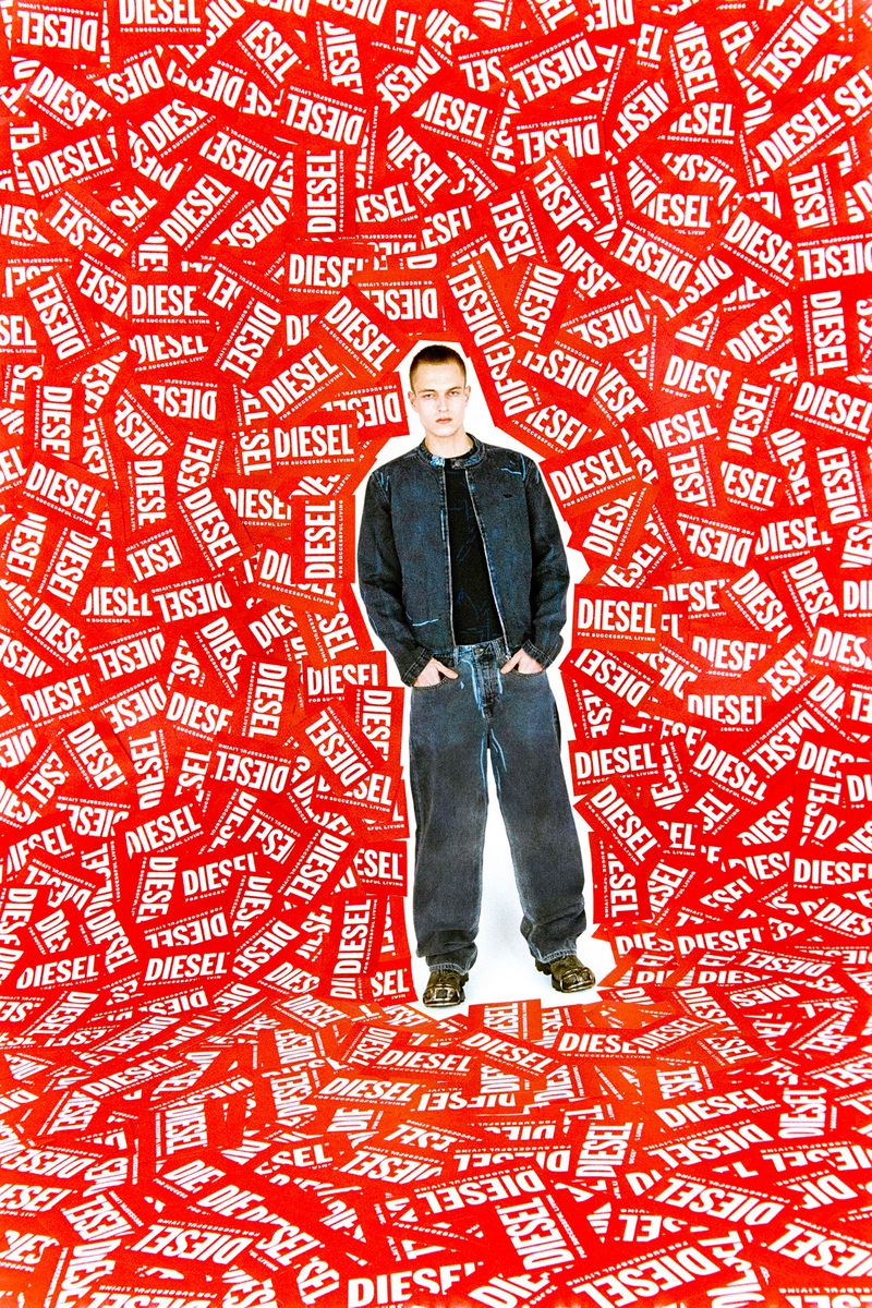A full-length shot of a man wearing a jacket and jeans, standing against a backdrop densely covered with 'Diesel' logo signs.