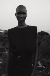 Black and white portrait of a model with short hair wearing a dark top against a rocky coastal background