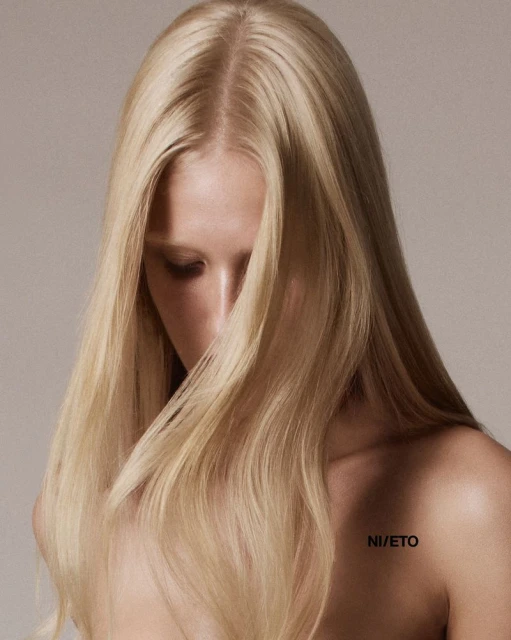 Close-up studio shot of a young adult woman with long blonde hair. The soft lighting highlights her features against a neutral backdrop.