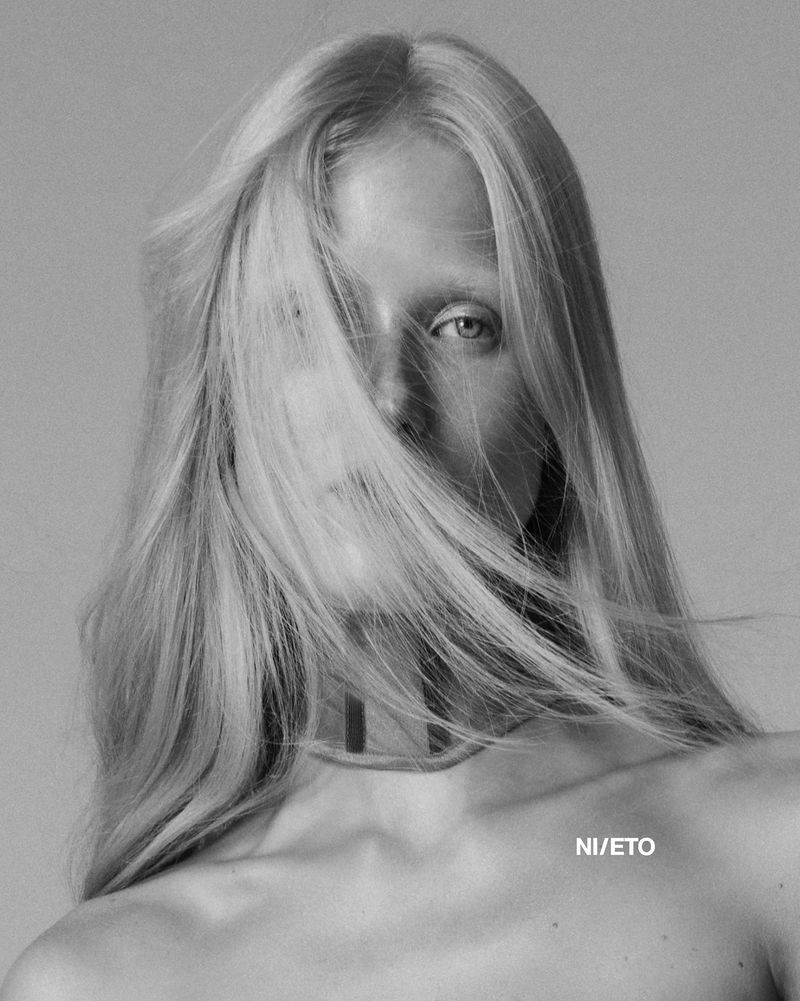 Black and white portrait of an adult female with long blonde hair partially covering her face, shot in a photo studio setting.