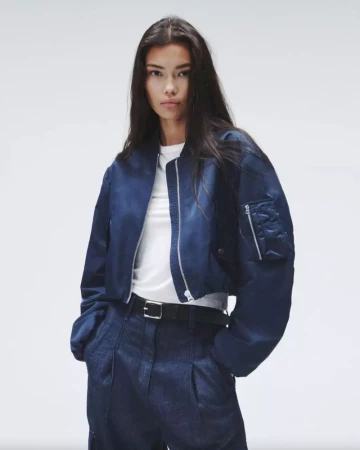 Young woman poses in a navy bomber jacket and matching trousers against a plain white backdrop in a studio fashion shot.