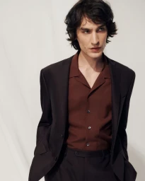 Model wearing dark suit jacket and brown button-up shirt against a plain white studio background.