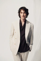 Model Valerio Maccario wearing a cream double-breasted tailored suit jacket over a black shirt against a white backdrop.