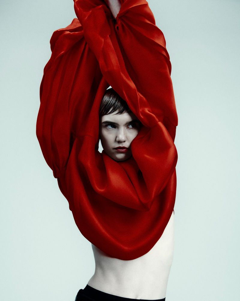 Artistic studio portrait of a woman draped in flowing red fabric, emphasizing dramatic lighting and a striking visual narrative.