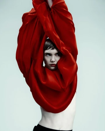 Artistic studio portrait of a woman draped in flowing red fabric, emphasizing dramatic lighting and a striking visual narrative.