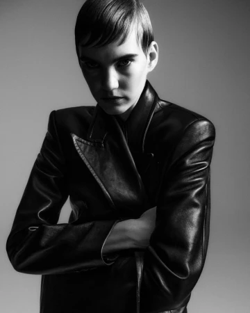 Model Ilya Vermeulen poses in a structured black leather coat with arms crossed in a monochrome studio portrait for Khaite.