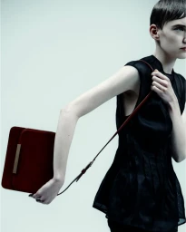 Model wearing a black sleeveless top carrying a structured red leather handbag against a pale seamless backdrop.