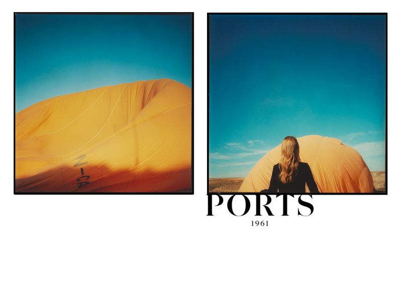 Fashion shot featuring a woman in a black jacket standing in front of a large, deflated yellow hot air balloon under a clear blue sky.