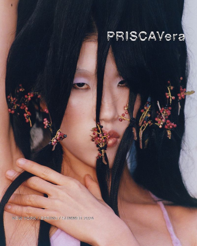 Asian female model in close-up studio fashion shot with ornate dark hair, floral hair accessories, and minimal makeup in a magazine cover style.