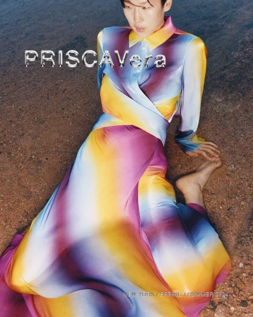 Editorial shot of a person in a colorful silk dress, lying on sand with a glossy magazine aesthetic. The dress features blue, pink, and yellow tones.