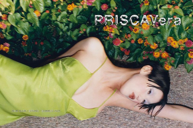 Woman in a light green dress lying on the ground next to vibrant flowers. Fashion editorial image for Priscavera New York collection.