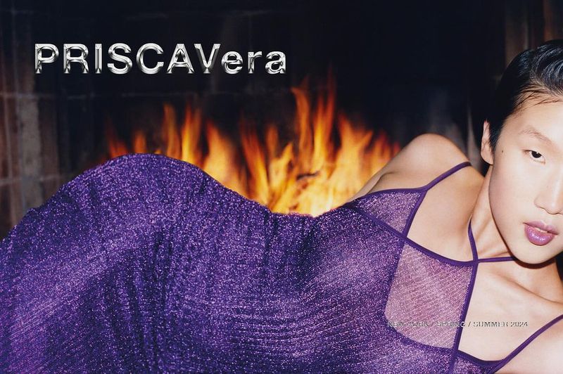 Woman in purple dress poses in front of fireplace. Fashion shot with indoor setting and dominant colors of orange, brown, and purple.