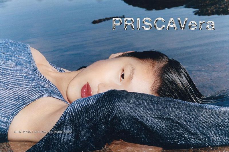 Fashion shot of a woman in a denim top lying on a wet surface near water, featuring a close-up with PriscaVera text overlay.