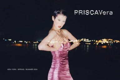 Model Jiashan Liu wears a metallic pink strapless dress against a dark body of water with blurred city lights at night.