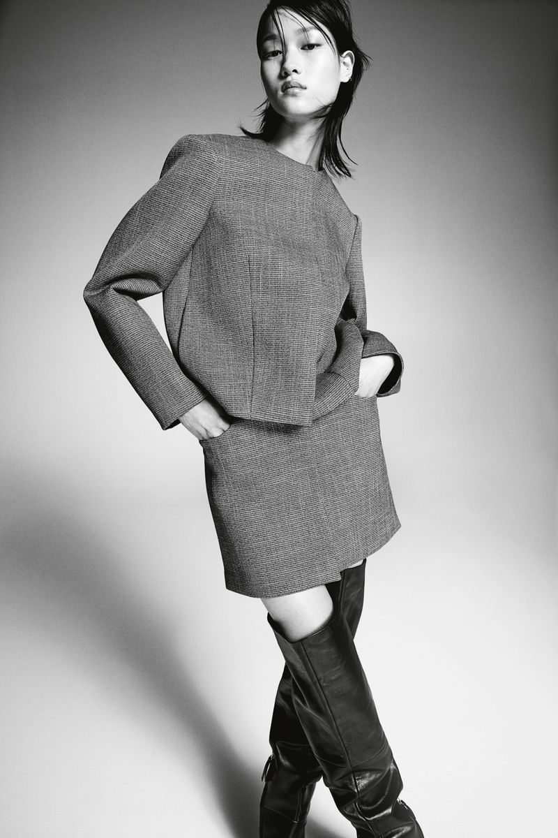 Model in grey tailored co-ord skirt suit and dark knee-high boots posing against a neutral gradient backdrop