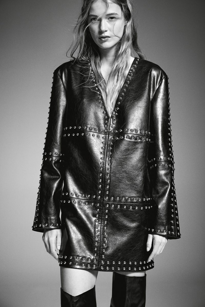 Studio shot of a woman in a studded black leather jacket dress and knee-high boots, showcasing a high-fashion editorial aesthetic.
