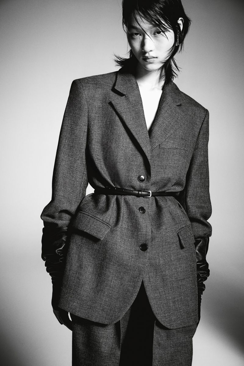 Model in grey blazer and black gloves posing against a grey seamless background for H&M