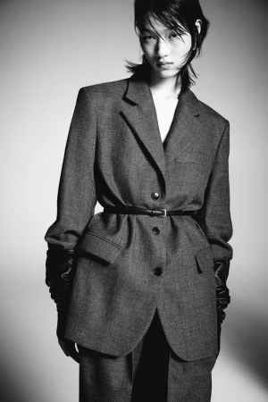 Model in grey blazer and black gloves posing against a grey seamless background for H&M