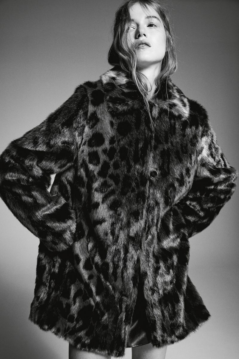 Woman wearing a black and brown leopard print faux fur coat looking up in a studio with a grey seamless background.