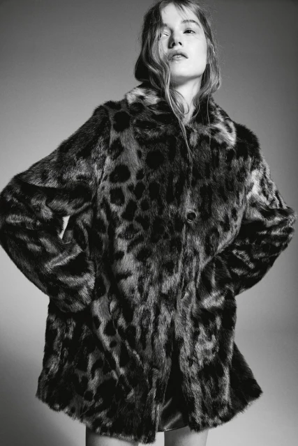 Woman wearing a black and brown leopard print faux fur coat looking up in a studio with a grey seamless background.