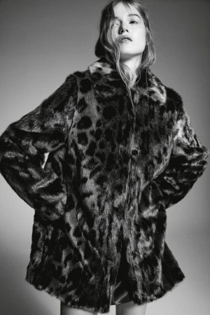 Woman wearing a black and brown leopard print faux fur coat looking up in a studio with a grey seamless background.