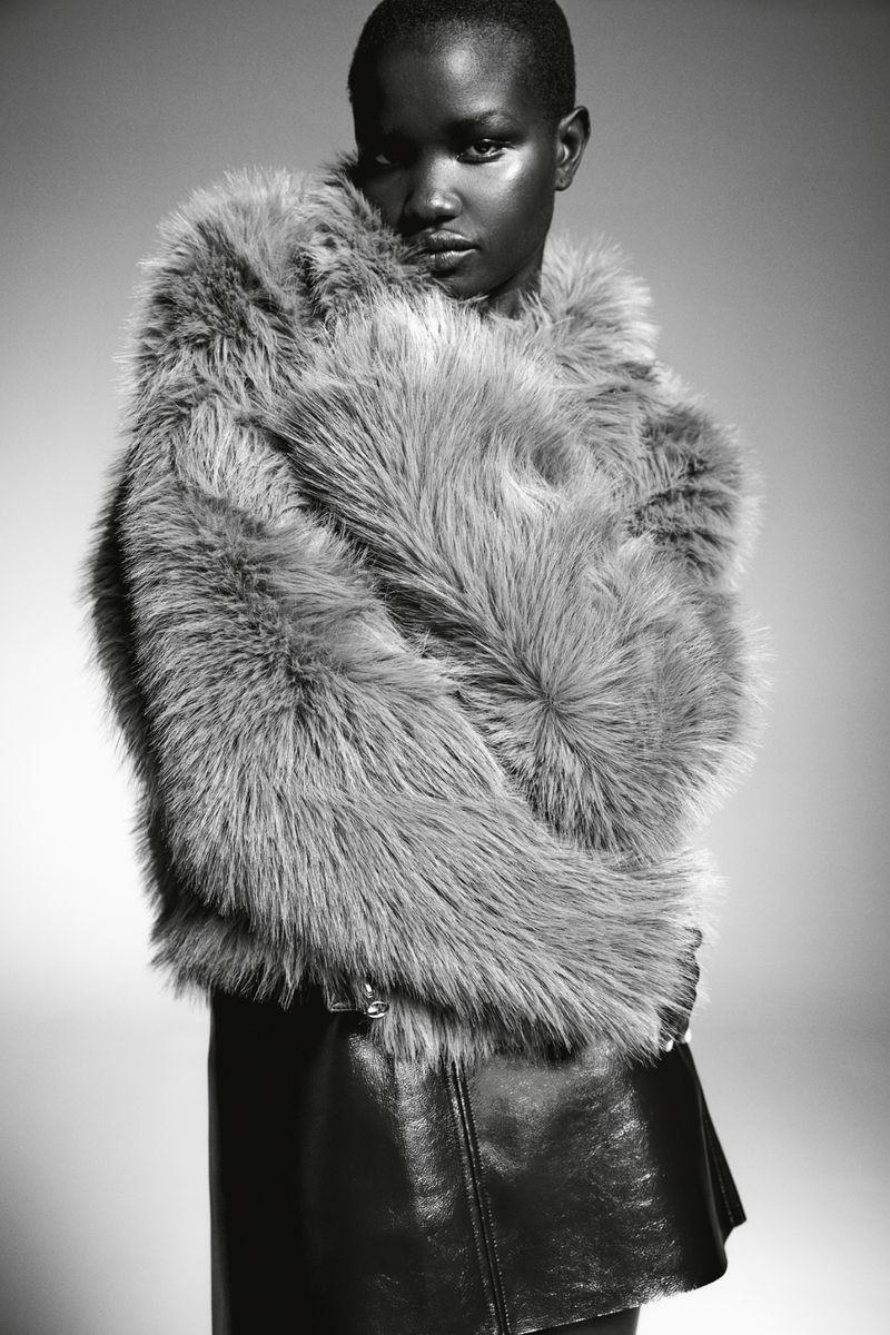 Monochrome portrait of a Black woman with short hair wearing a furry grey coat and black skirt against a neutral background.