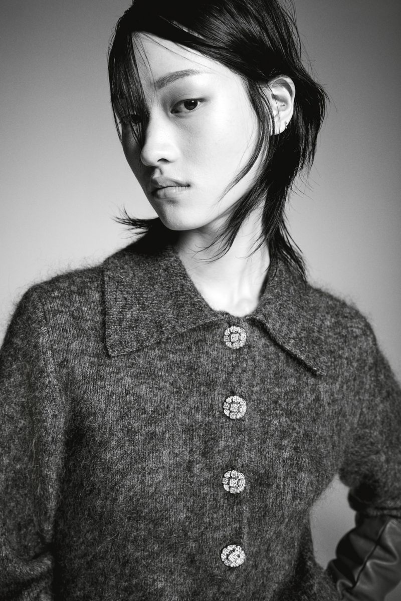Monochrome portrait of an Asian woman with dark hair wearing a textured grey collared jacket with decorative crystal buttons in studio.
