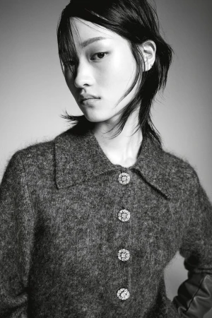 Monochrome portrait of an Asian woman with dark hair wearing a textured grey collared jacket with decorative crystal buttons in studio.