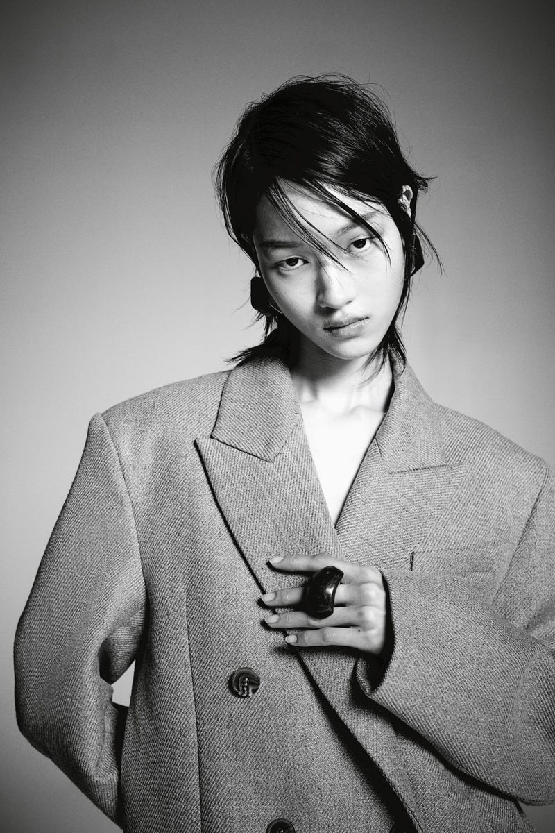 Portrait of a stylish Asian woman in a grey double-breasted blazer, posing against a grey backdrop, showcasing a modern fashion look.