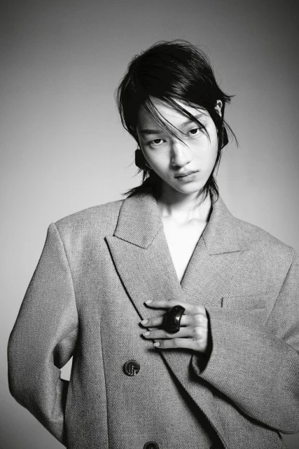 Portrait of a stylish Asian woman in a grey double-breasted blazer, posing against a grey backdrop, showcasing a modern fashion look.