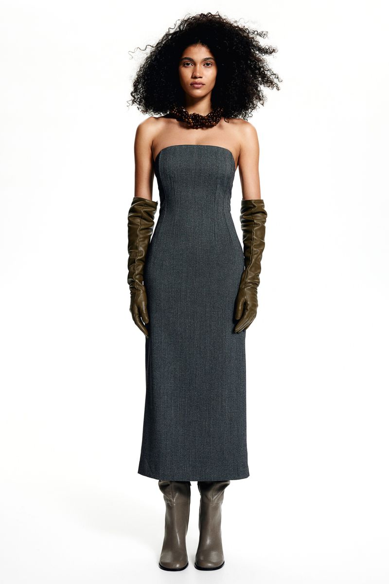 Model wearing a strapless charcoal midi dress, olive leather gloves, and grey boots against a white background