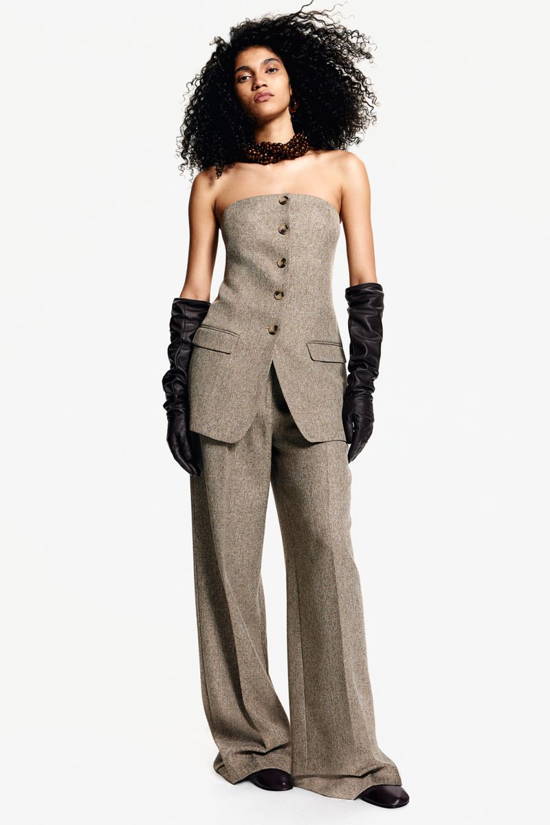 Model in strapless beige tweed top and matching trousers wearing black leather opera gloves against a white seamless backdrop